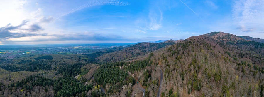 A mountainous landscape with dense forests, a winding road, and a distant view of a town.