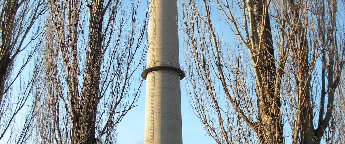 A tall chimney with a red and white top, surrounded by leafless trees.