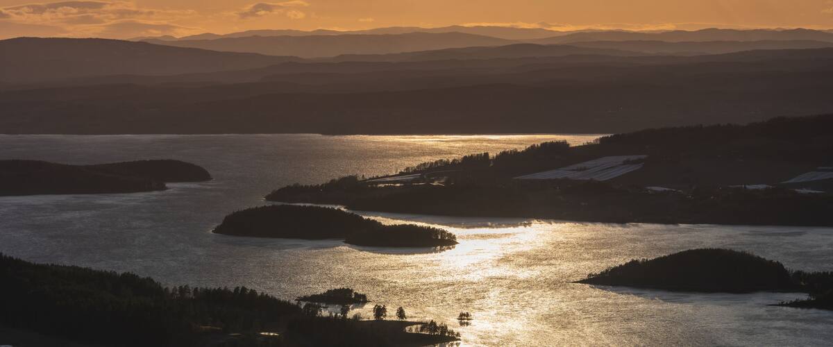 A lake surrounded by forested hills during sunset.
