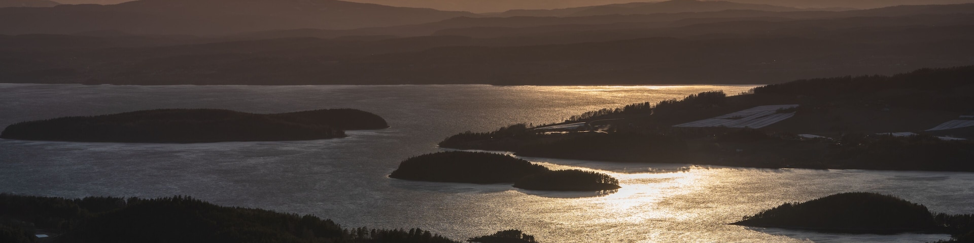 A lake surrounded by forested hills during sunset.