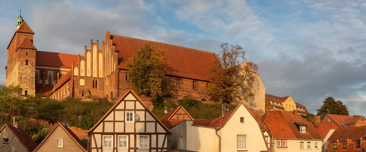 A historic church with a tall bell tower and a medieval castle in the background.