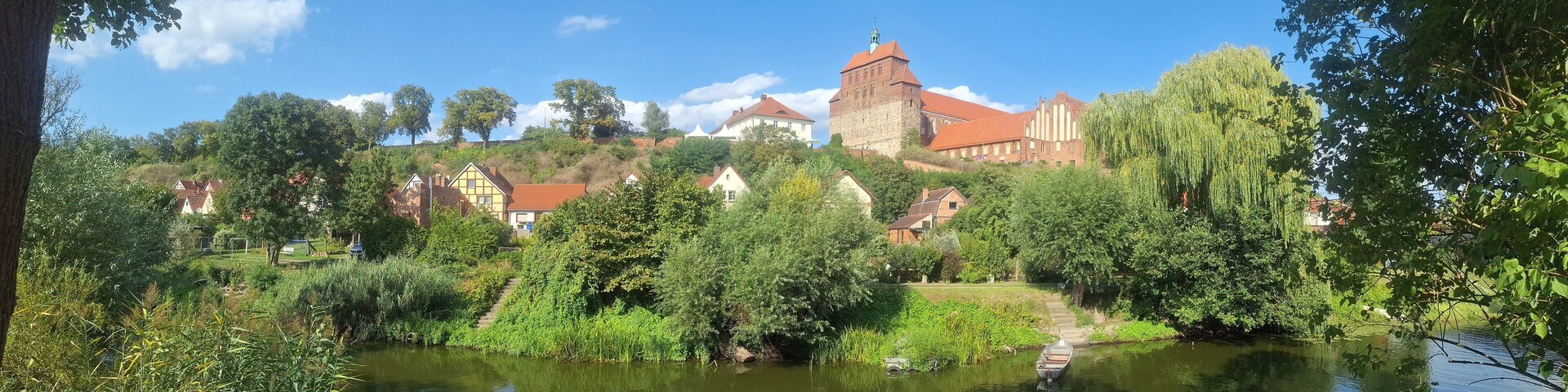 Un pueblo histórico con un castillo imponente, un río y abundante vegetación.