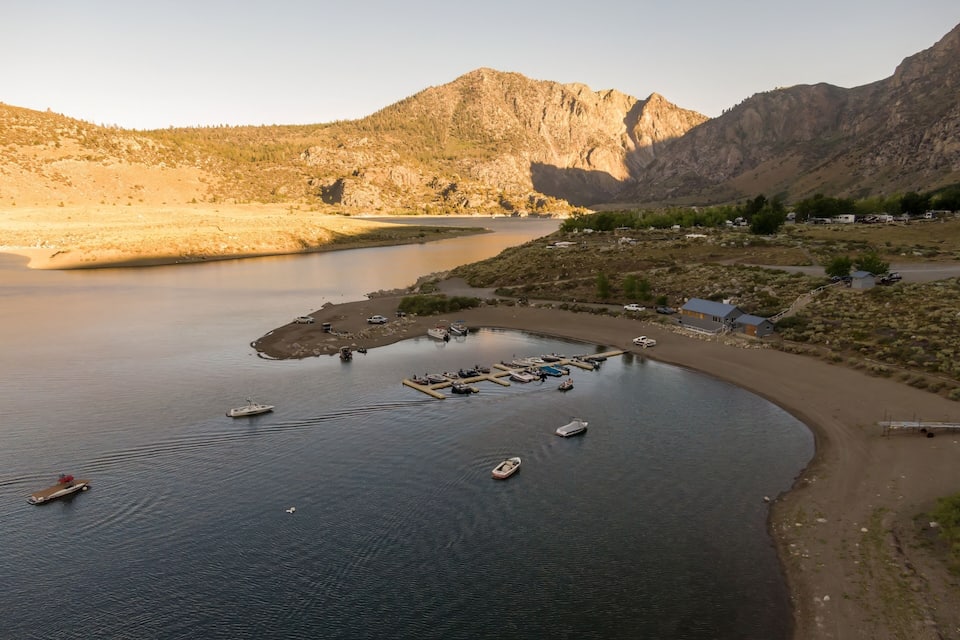 Un lago tranquilo con barcos amarrados en un pequeño muelle, rodeado de montañas y vegetación escasa.
