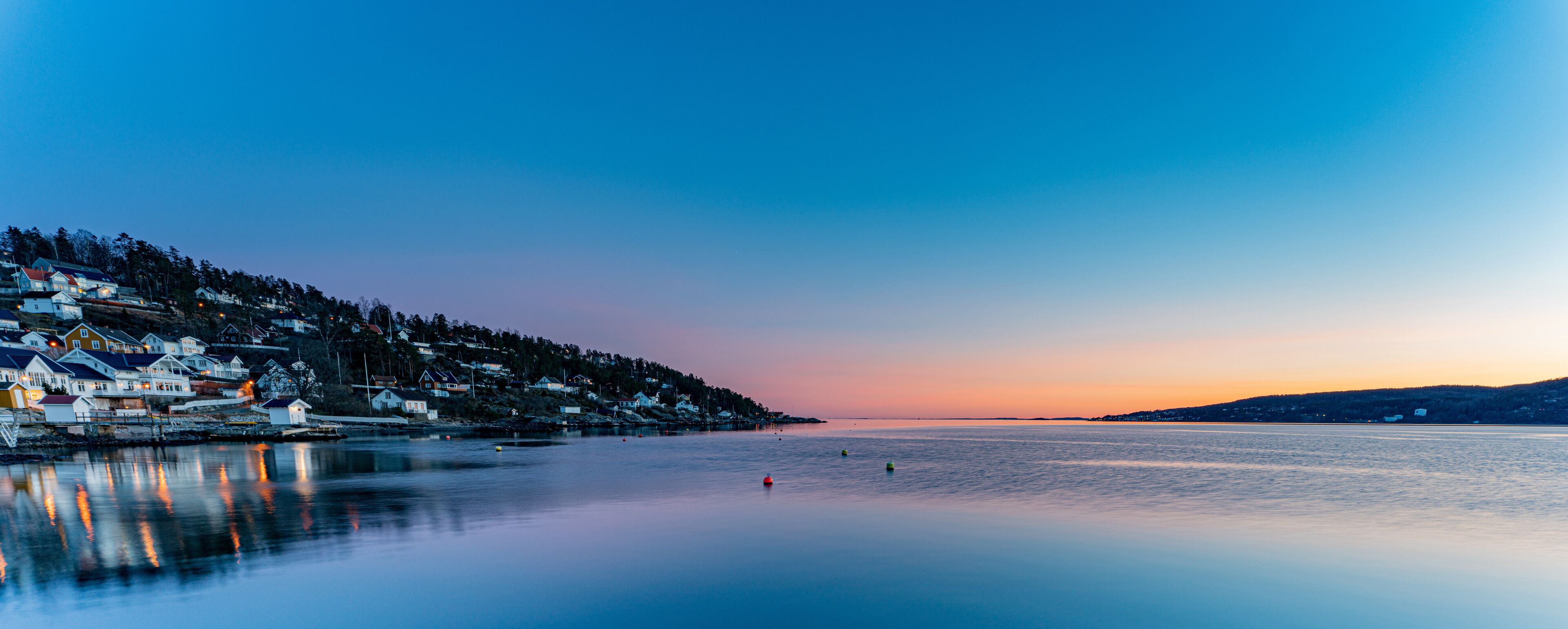 A coastal town at dusk with houses along the shoreline and calm waters.