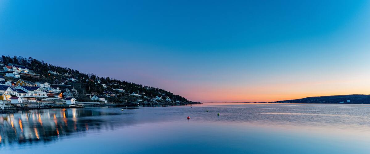 A coastal town at dusk with houses along the shoreline and calm waters.