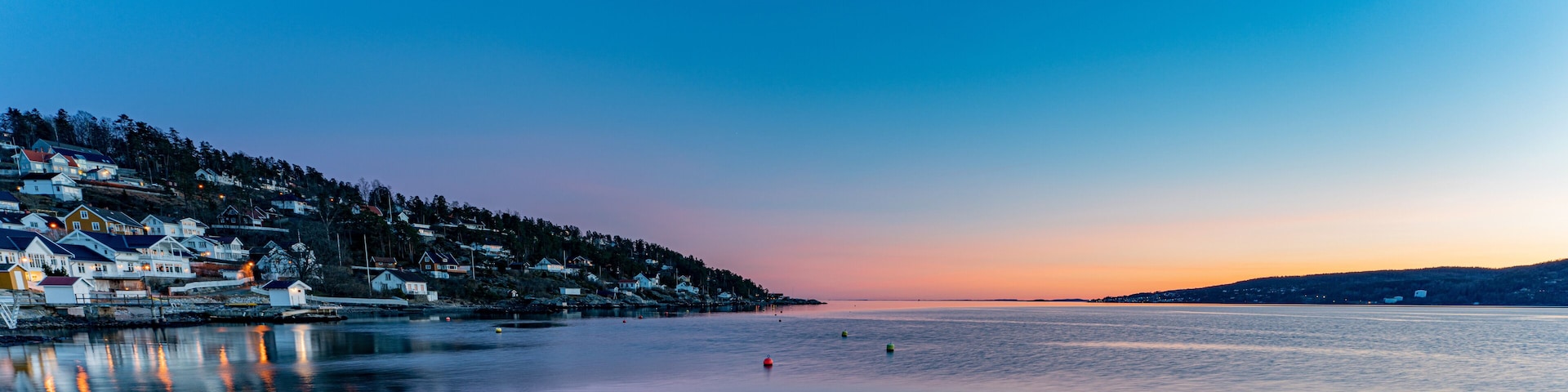 A coastal town at dusk with houses along the shoreline and calm waters.