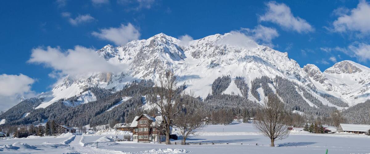 A snow-covered mountain range with a chalet and a clear blue sky.