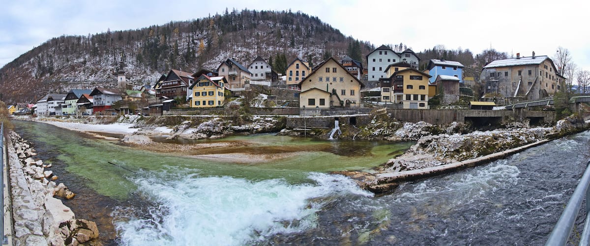 A river flowing through a town with colorful houses and a mountainous backdrop.