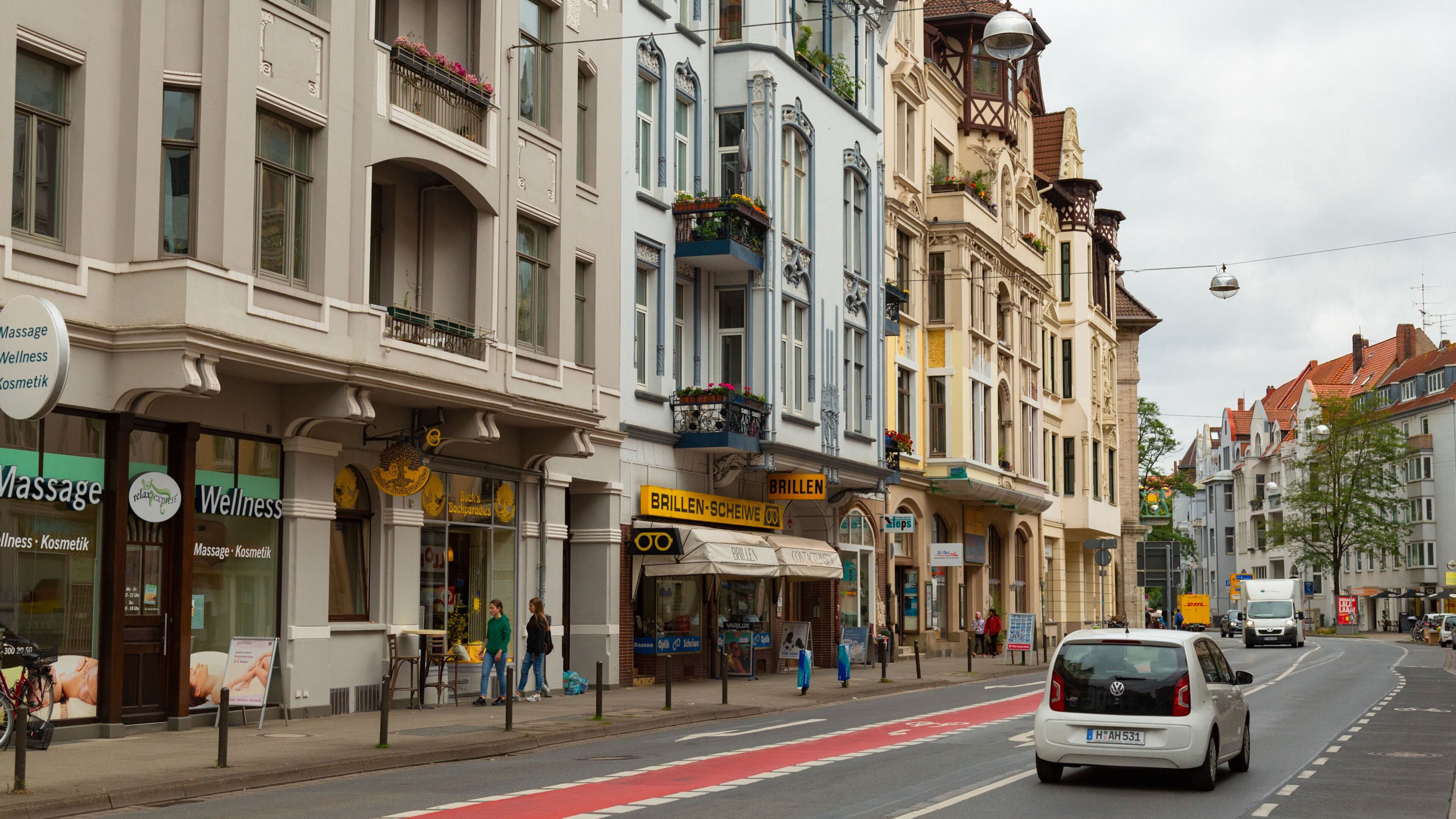 Una calle con edificios de estilo europeo, tiendas y un coche blanco circulando.