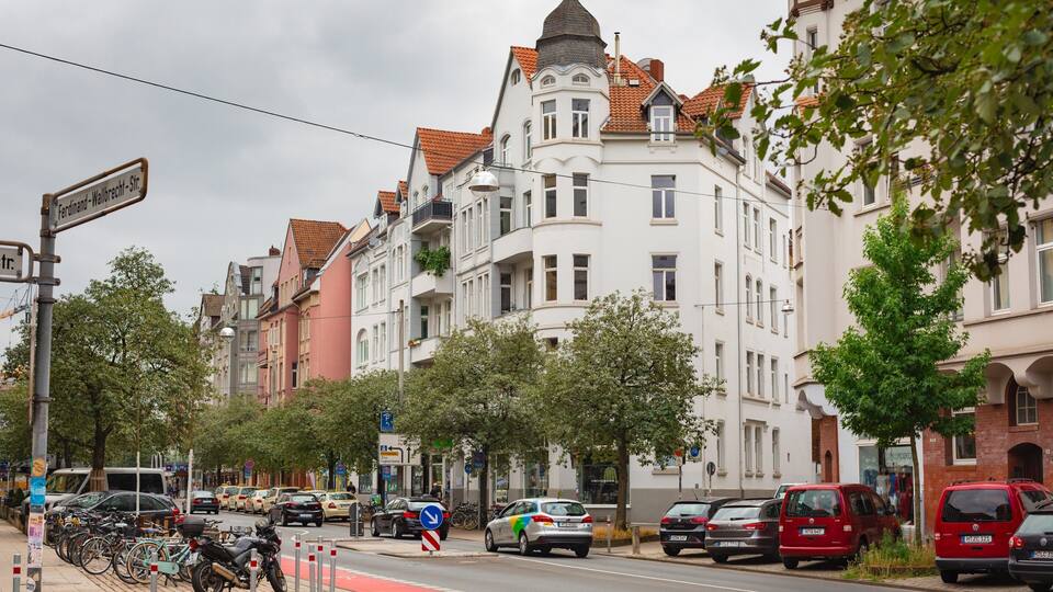 Eine Straße mit parkenden Autos, Fahrrädern und einem Gebäude mit roten Ziegeldach.