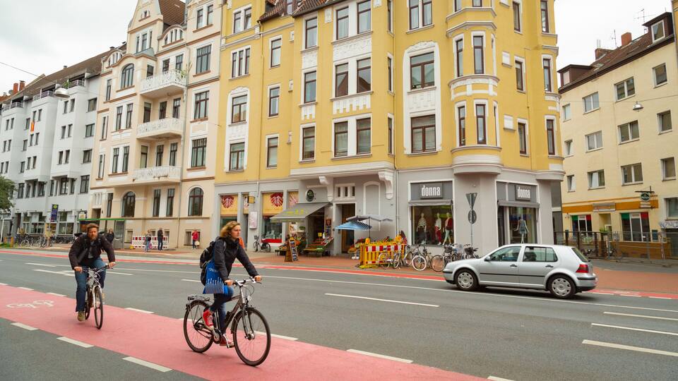 A street with cyclists, a car, and buildings with shops.
