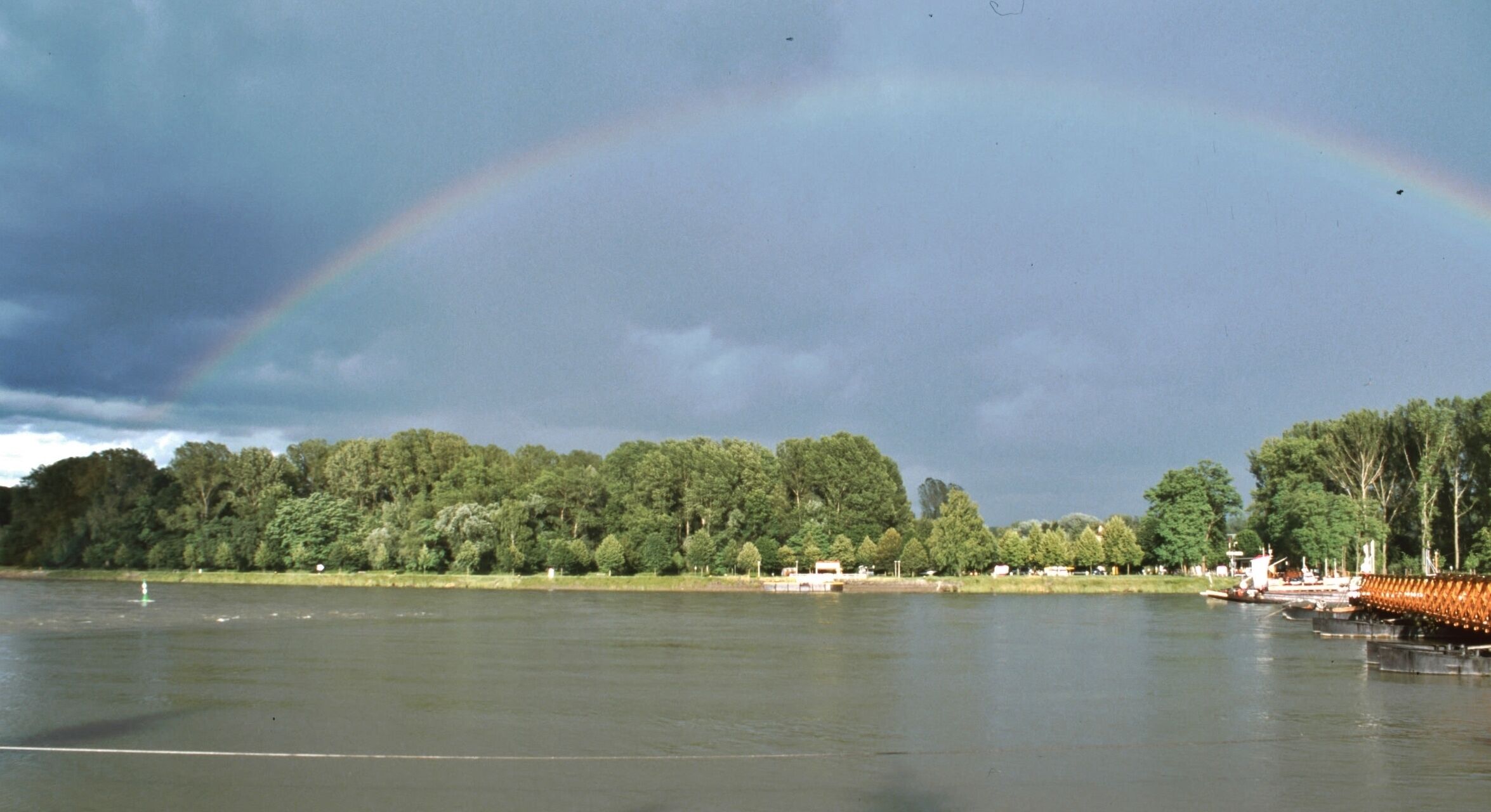 A lake with a rainbow, trees, and a dock.