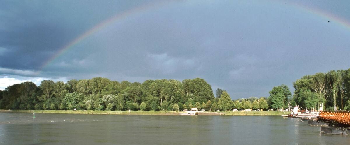 A lake with a rainbow, trees, and a dock.