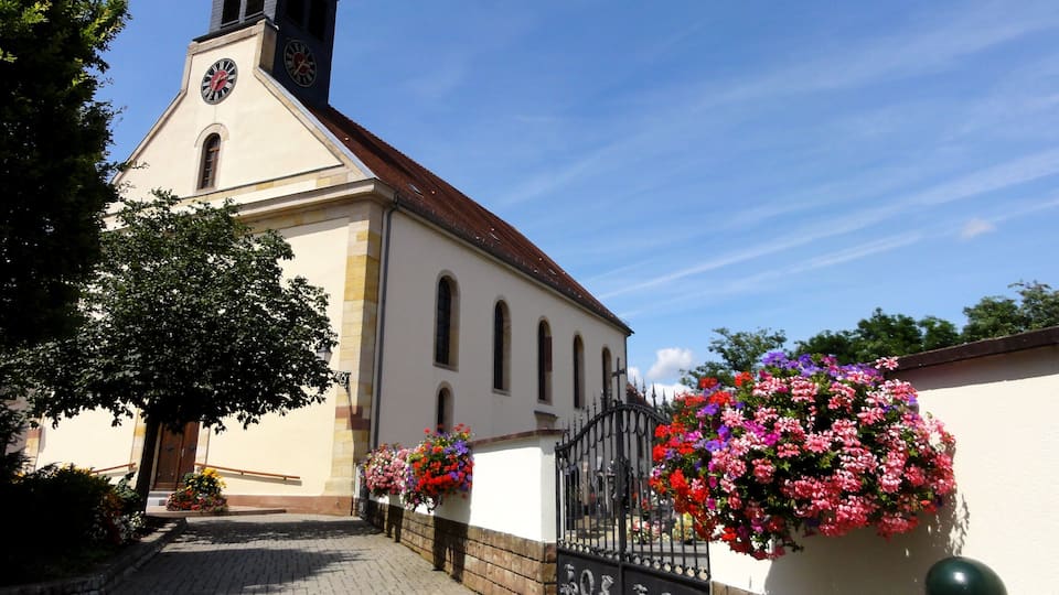 A church with a clock tower, a paved pathway, and flower baskets.