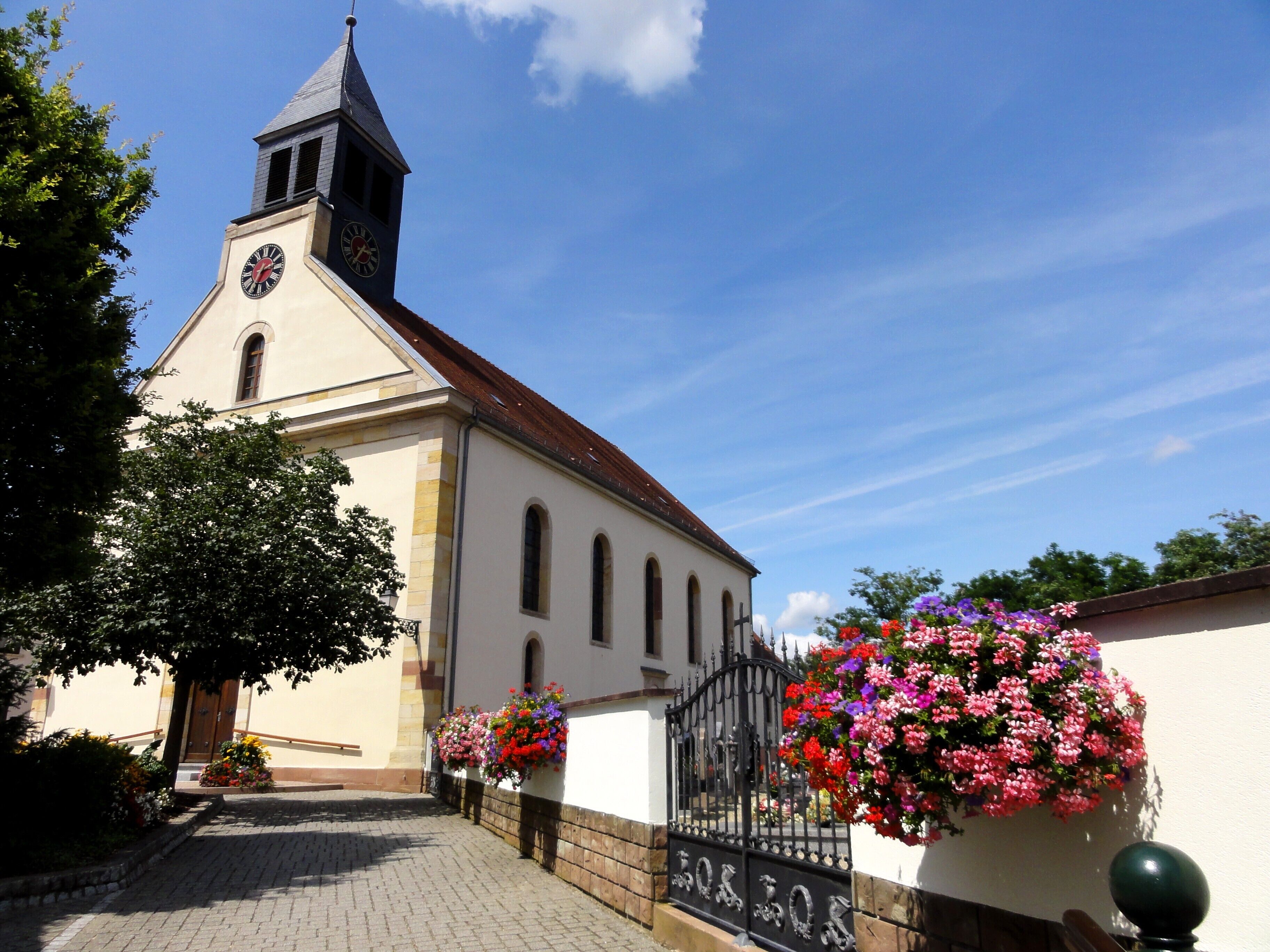 A church with a clock tower, a paved pathway, and flower baskets.