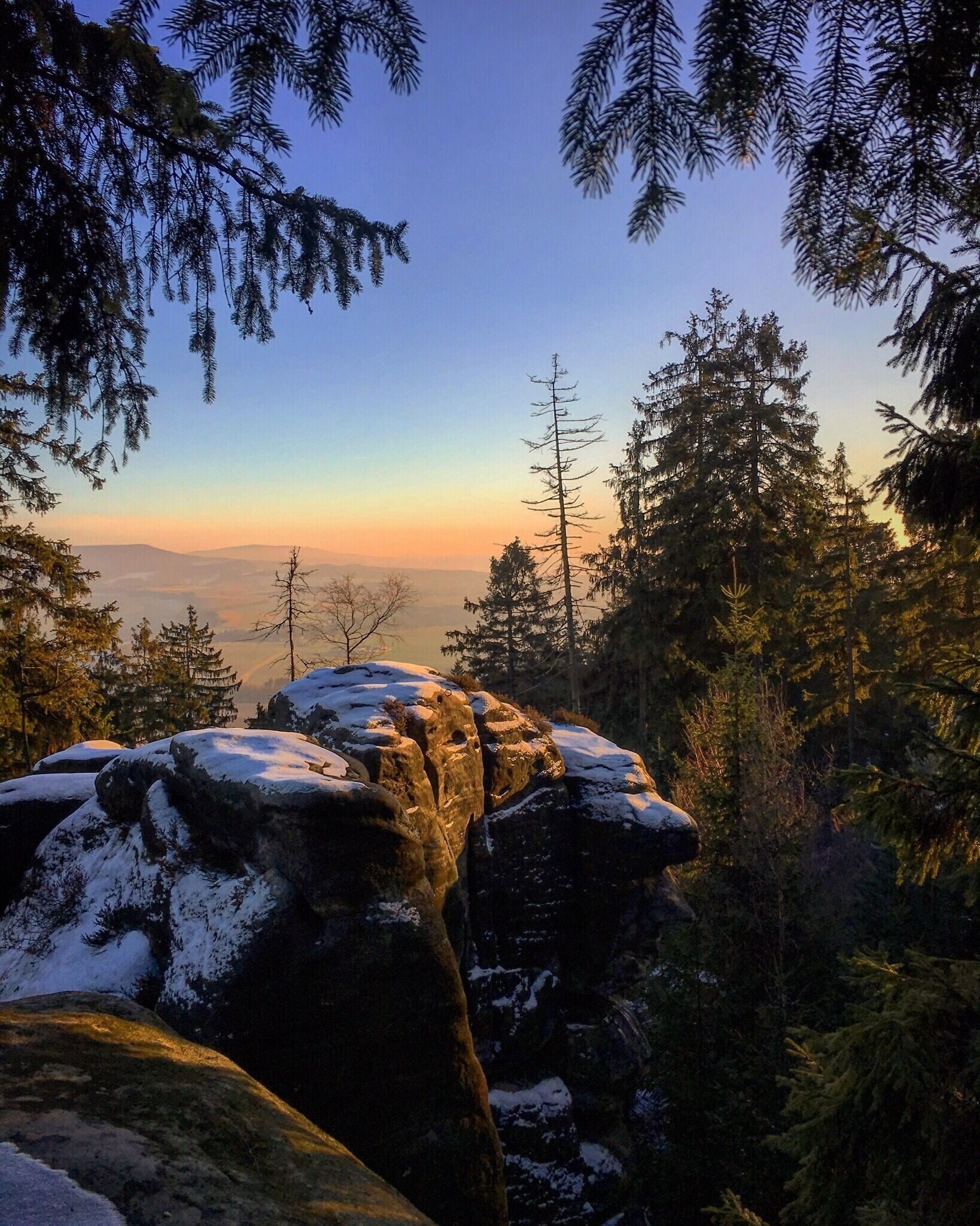 A snow-covered rock formation with a forest and distant mountains.