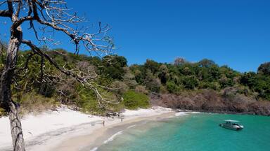 A beach with clear turquoise water, white sand, and a boat in the distance.
