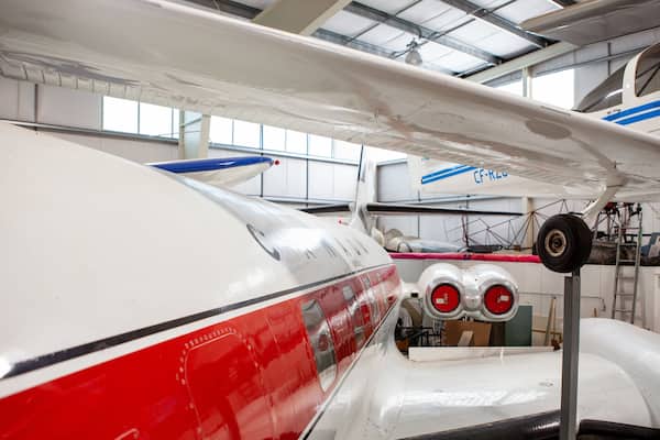 Un avion blanc et rouge avec des bandes bleues, une hélice et une dérive rouge, garé dans un hangar.