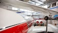 A white and red airplane with blue stripes, a propeller, and a red tail fin in a hangar.