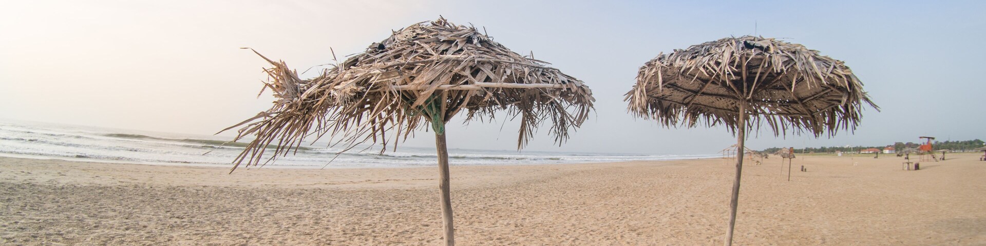 Two straw umbrellas on a sandy beach with the ocean in the background.