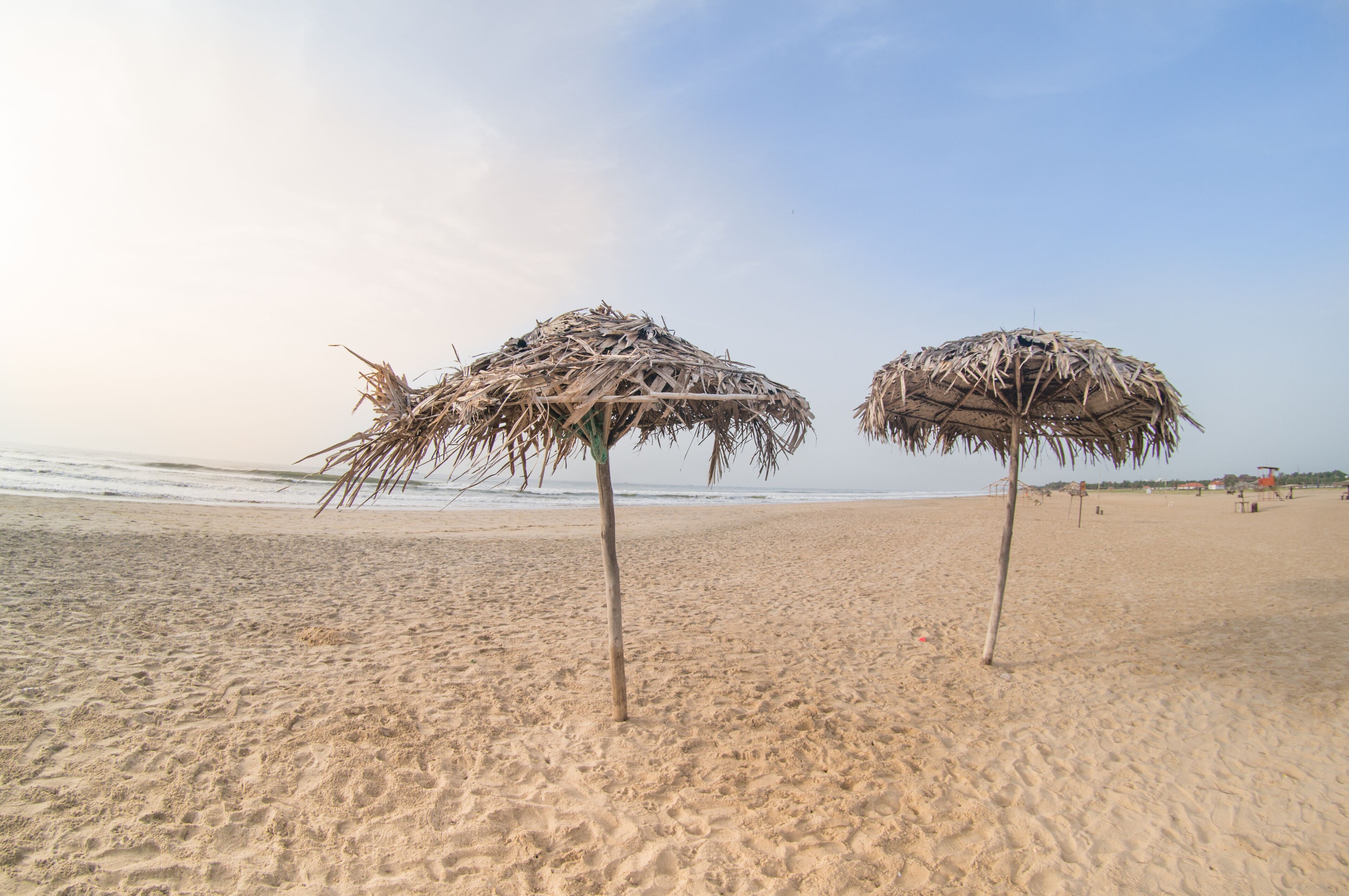 Two straw umbrellas on a sandy beach with the ocean in the background.