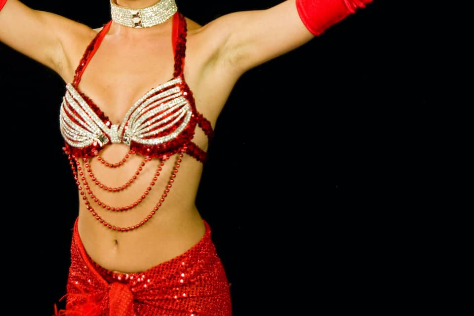 A person in a red and silver costume with a feathered headpiece and a beaded necklace.