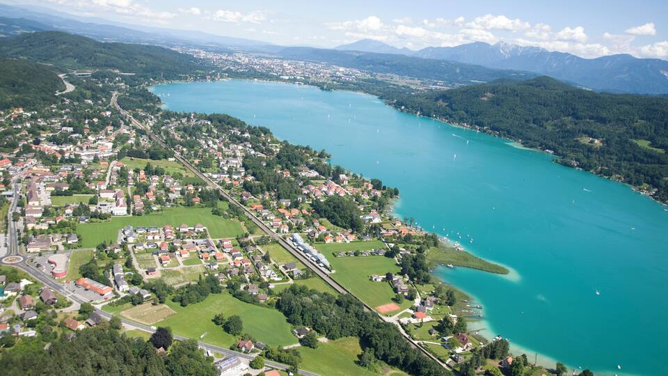 An aerial view of a town by a turquoise lake with surrounding mountains.