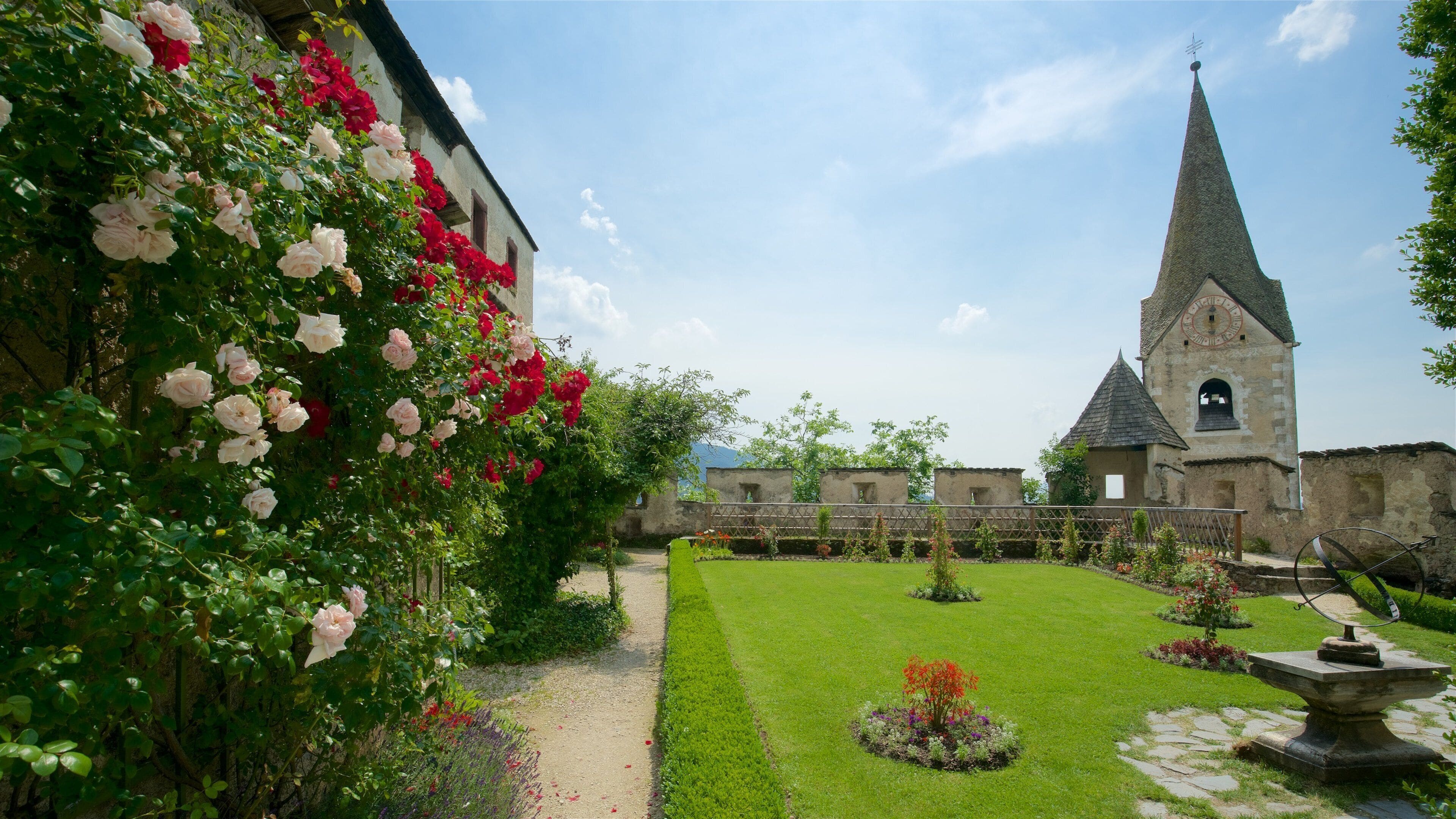 A garden with roses, a church, and a stone pathway.