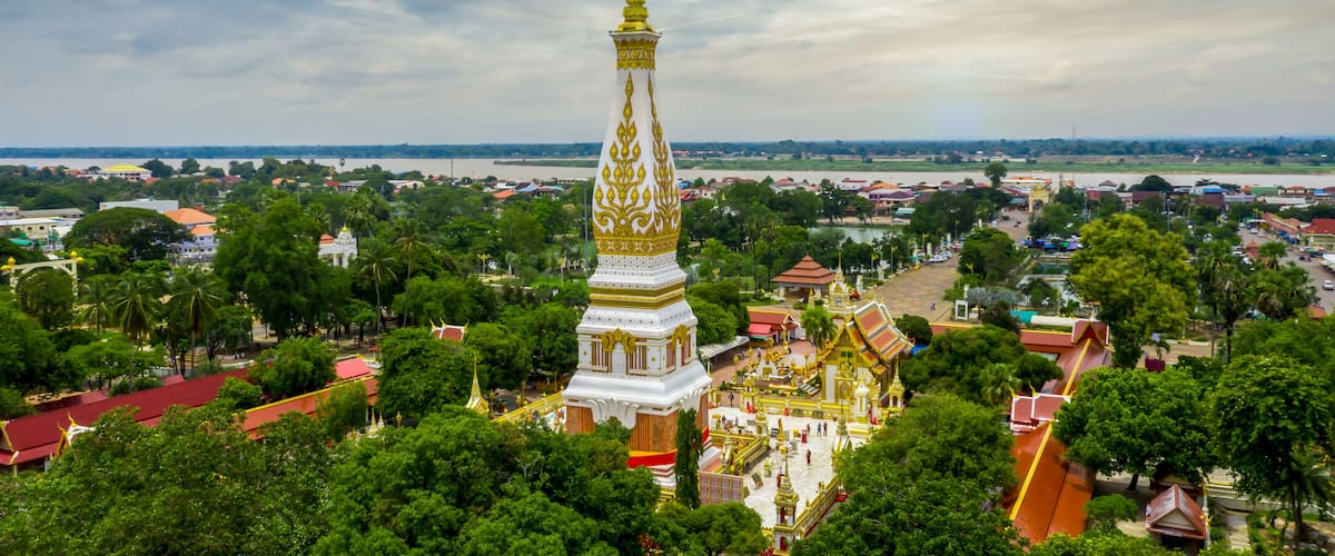 A temple with a tall spire and golden decorations, surrounded by lush green trees and a river in the background.