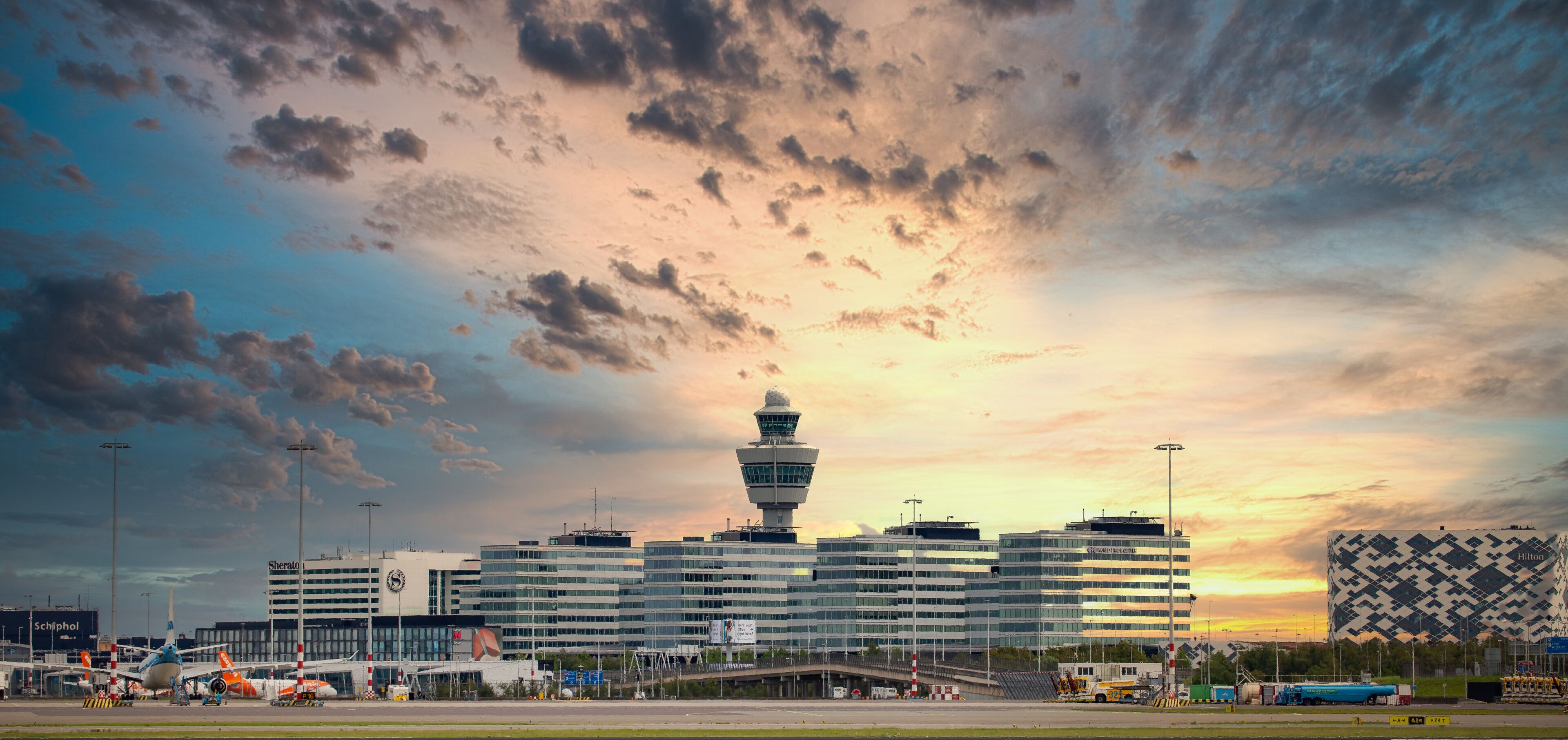 An airport with a control tower, terminal buildings, and a sunset sky.