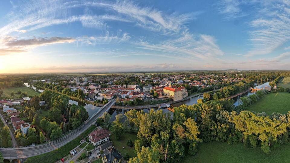 An aerial view of a town with a river, a bridge, and surrounding greenery.