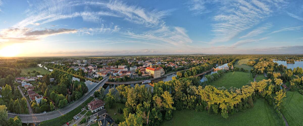 An aerial view of a town with a river, a bridge, and surrounding greenery.