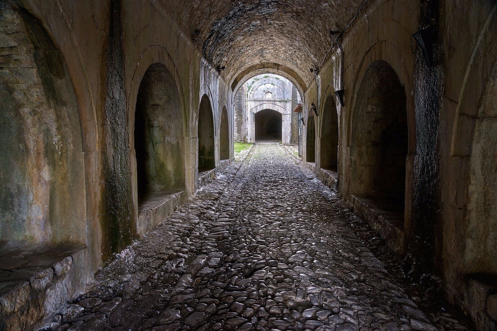 A stone pathway leading through an arched corridor with a cobblestone floor.