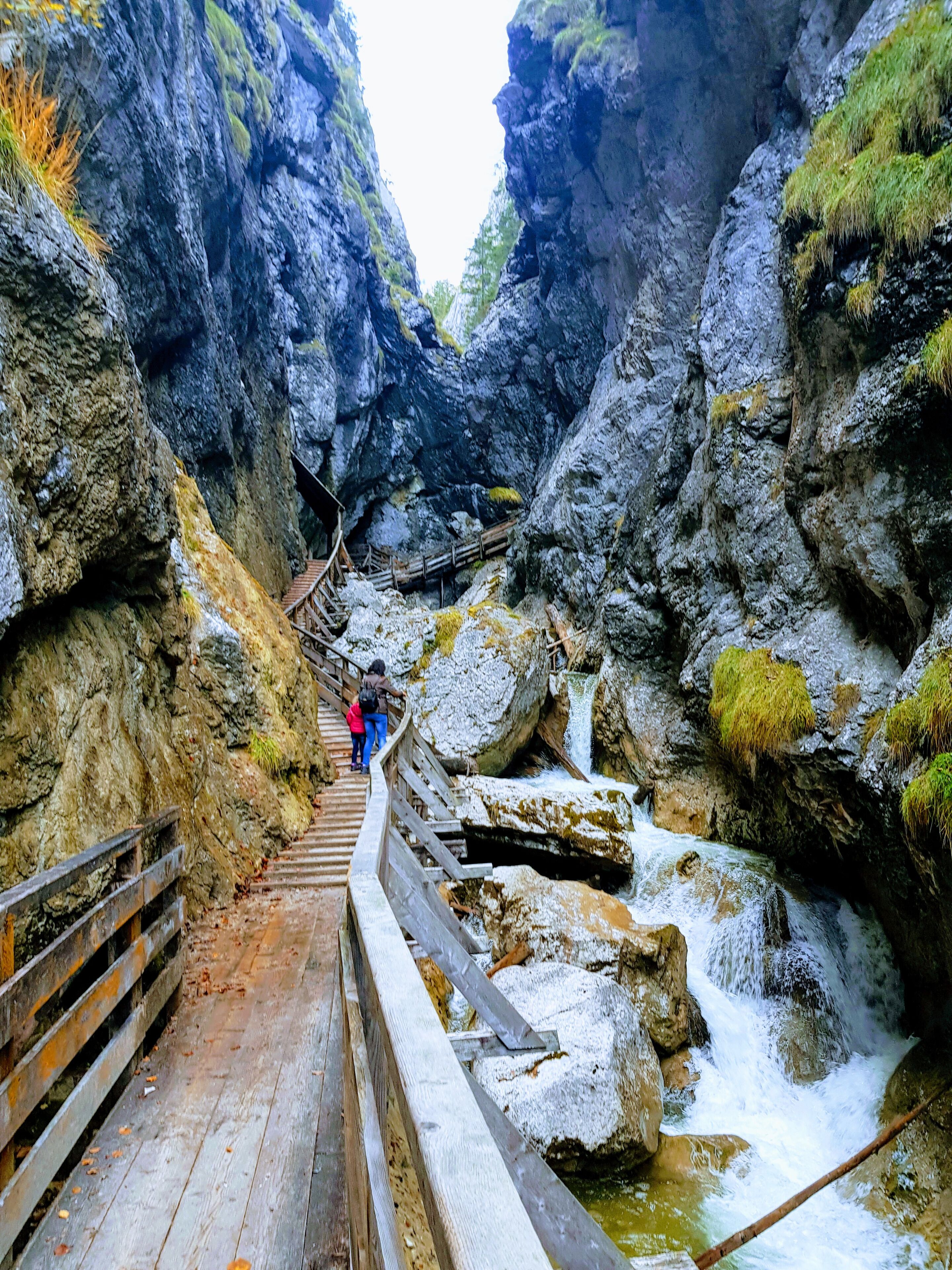 A wooden walkway leading through a rocky canyon with a waterfall.