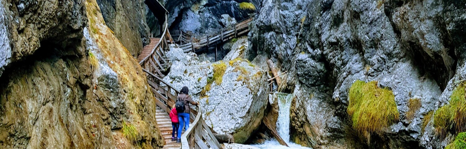 A wooden walkway leading through a rocky canyon with a waterfall.