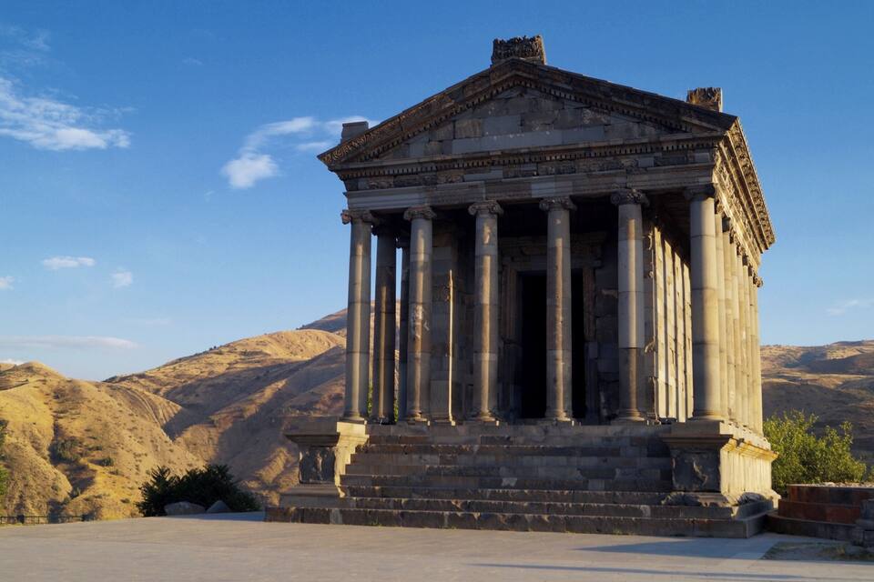 A classical temple with columns, set against a mountainous backdrop.