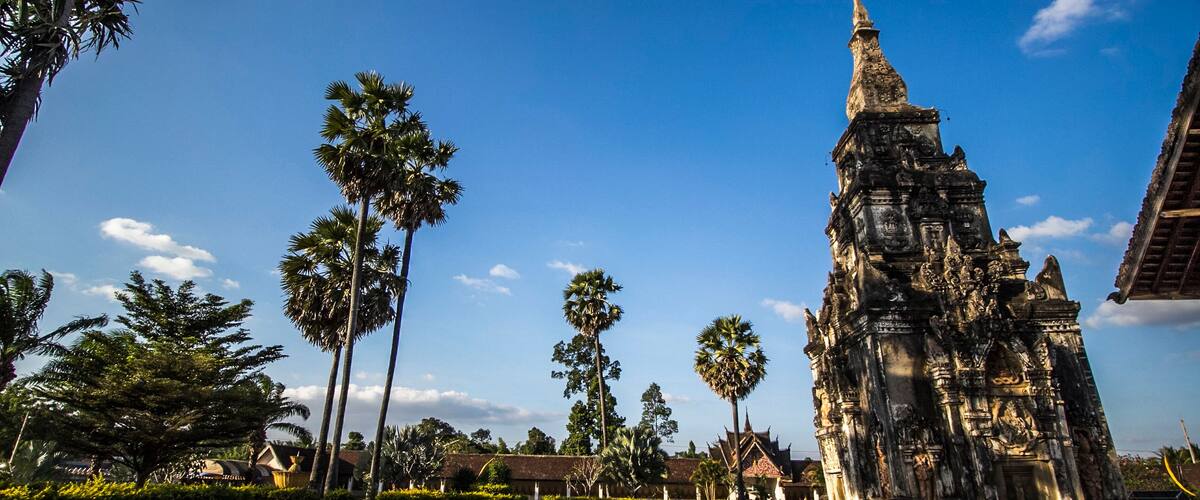A temple with intricate carvings and a tall spire, surrounded by palm trees and a clear blue sky.