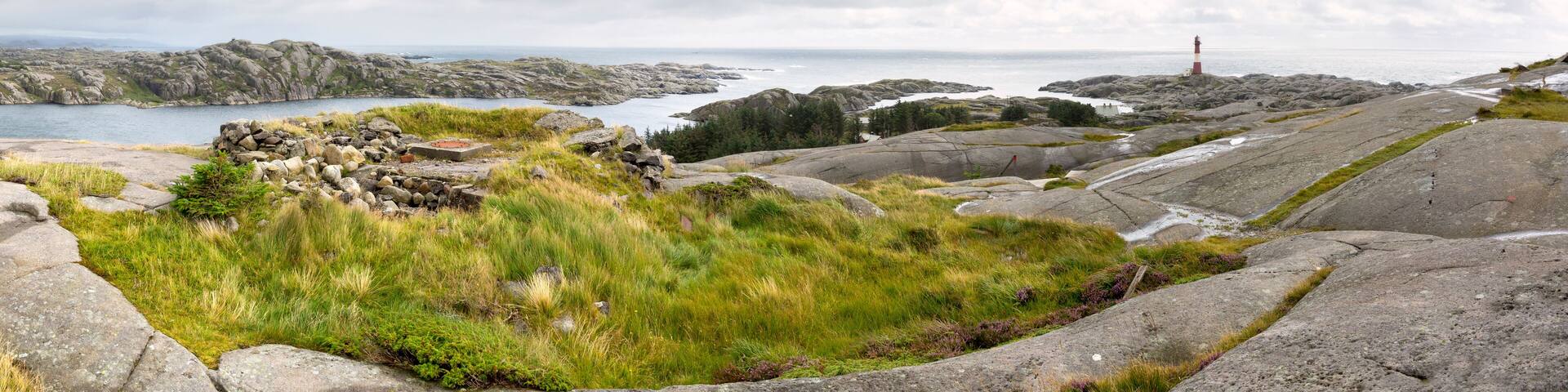 A rocky coastal landscape with a lighthouse in the distance.