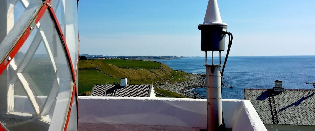 A coastal landscape with a lighthouse, grassy hills, and the sea.