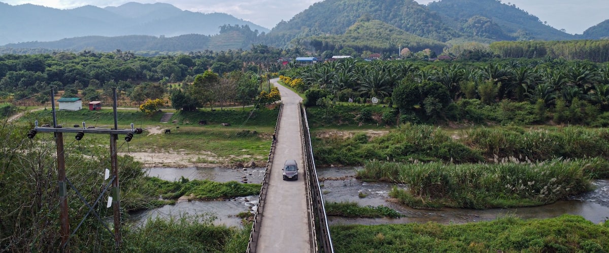 A bridge over a river with a car on it, surrounded by lush greenery and hills.