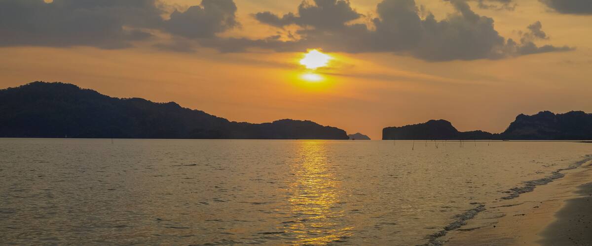 view panorama seaside evening on long beach of limestone mountain in the sea with yellow sun light and cloudy sky background, sunset at Pak Bara Beach, La-ngu District, Satun, southern Thailand.
