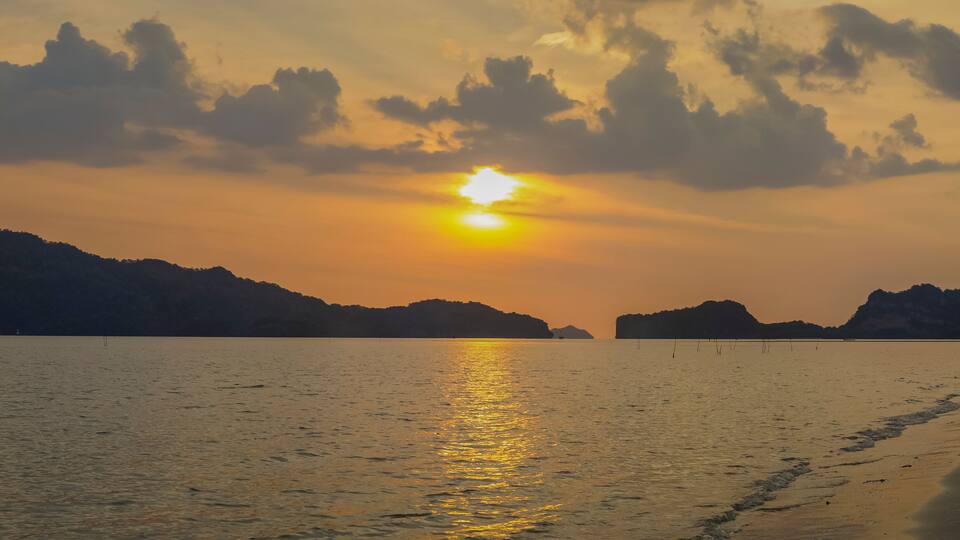 A sunset over a calm sea with distant landforms silhouetted against the sky.