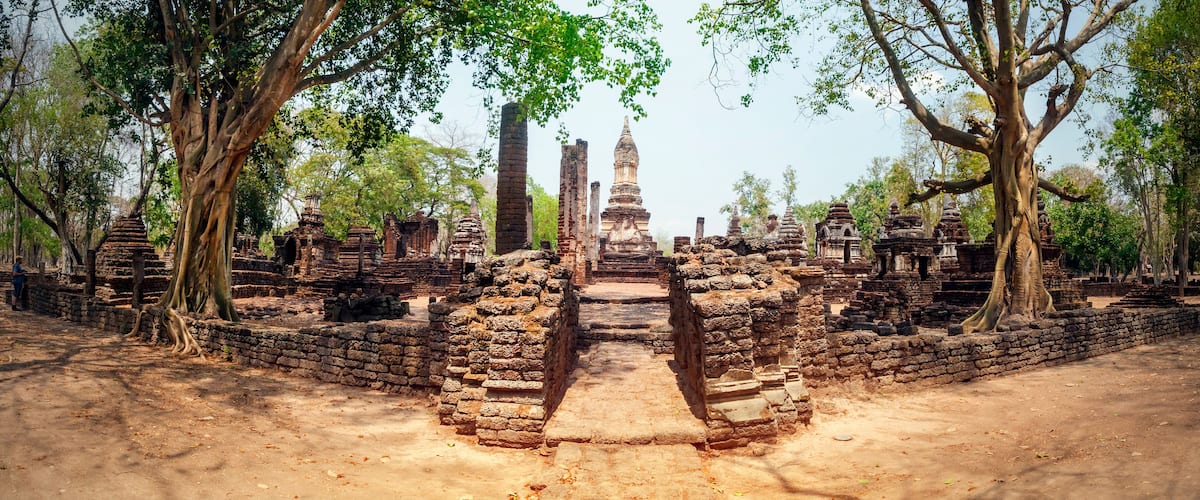 Ancient ruins with a central stupa surrounded by brick structures and trees.