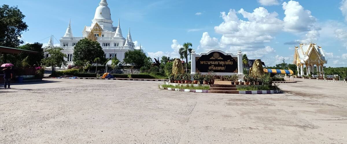 A large white temple complex with multiple spires, surrounded by greenery and a clear blue sky.