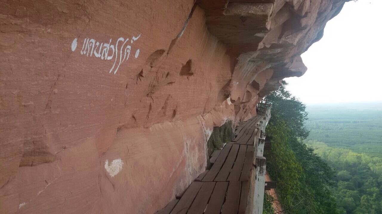 A red rock cliff with white markings and a wooden walkway.
