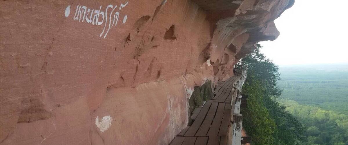A red rock cliff with white markings and a wooden walkway.