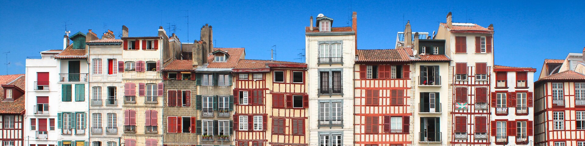 A row of colorful buildings with red and green shutters, under a clear blue sky.