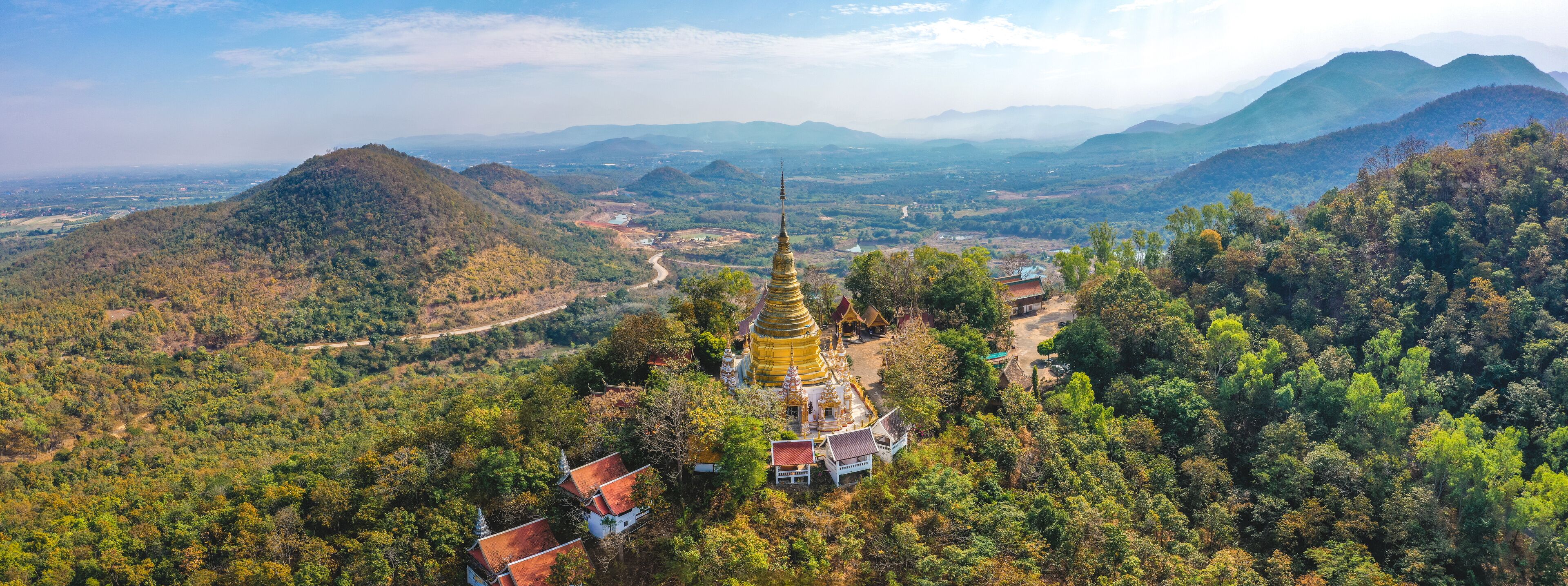 A golden pagoda surrounded by lush green hills and a winding road.