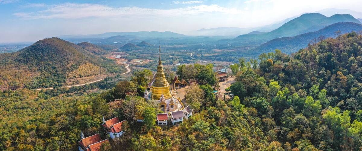 A golden pagoda surrounded by lush green hills and a winding road.