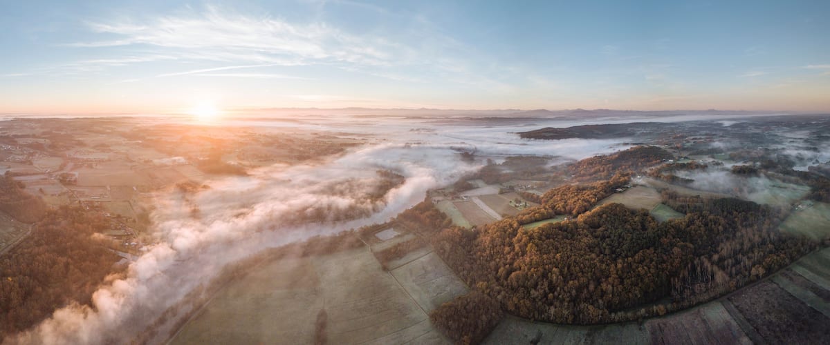 A vast landscape with rolling hills, fields, and a dense forest area.